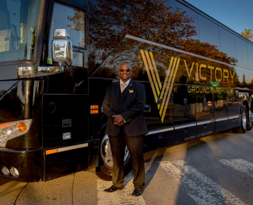 Front view of a smiling man standing in front of victory grounds charter bus