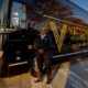 Front view of a smiling man standing in front of victory grounds charter bus