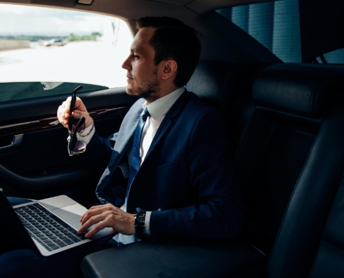 Business man working on laptop in the back of luxury car